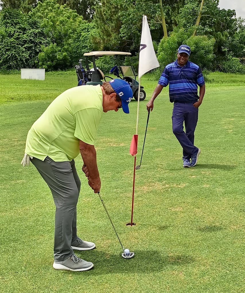 Two golfers on a green, one lining up a putt